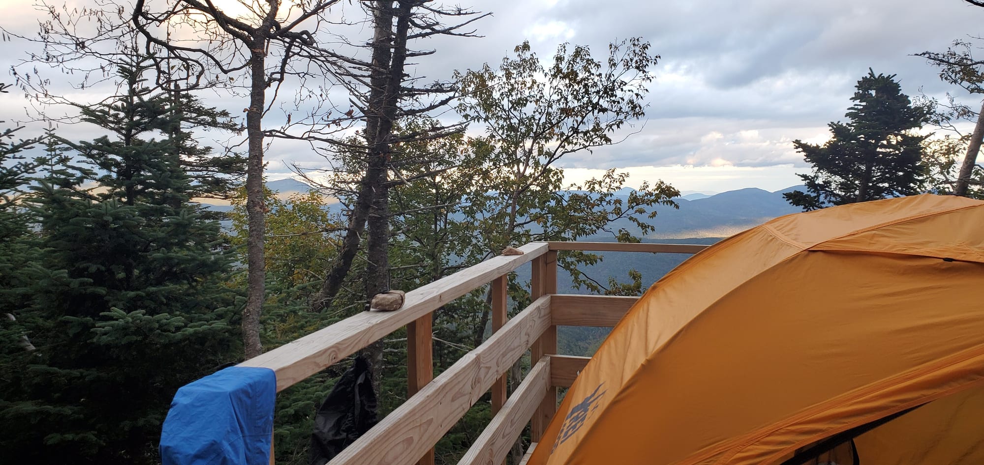 A tent pitched on a wooden backcountry tent platform at dusk, looking out over ridgelines